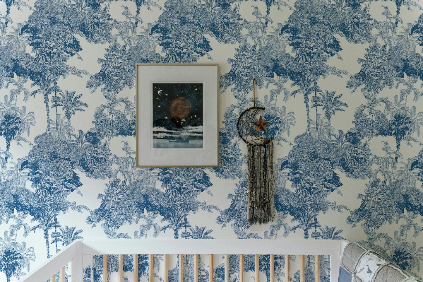 Nursery wallpaper with mountain and palm tree sketches above a white crib.