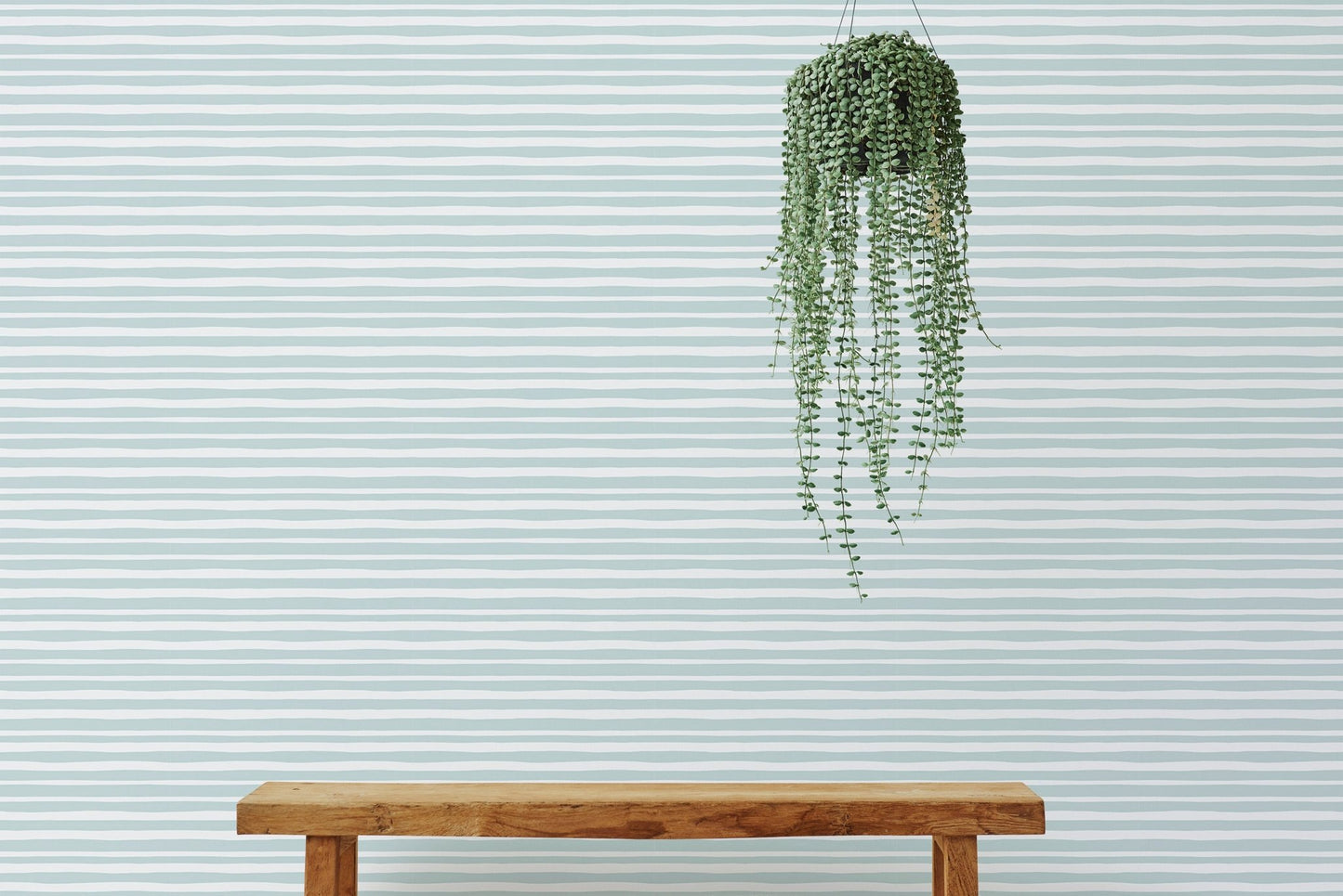 Simple wooden bench in front of a sea green horizontal striped wallpaper.