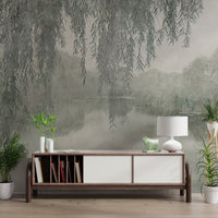 Hanging willow branches framing a misty lake and distant trees.