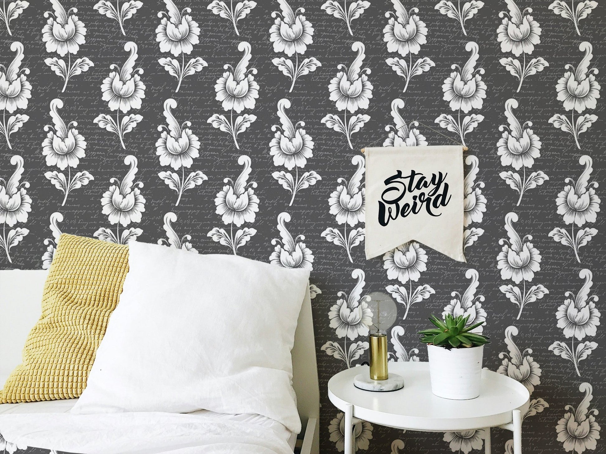 Monochrome leaf wallpaper behind a white bed with a yellow cushion.