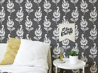 Monochrome leaf wallpaper behind a white bed with a yellow cushion.