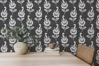 Black and white leaf wallpaper behind a light wood desk with a potted plant.