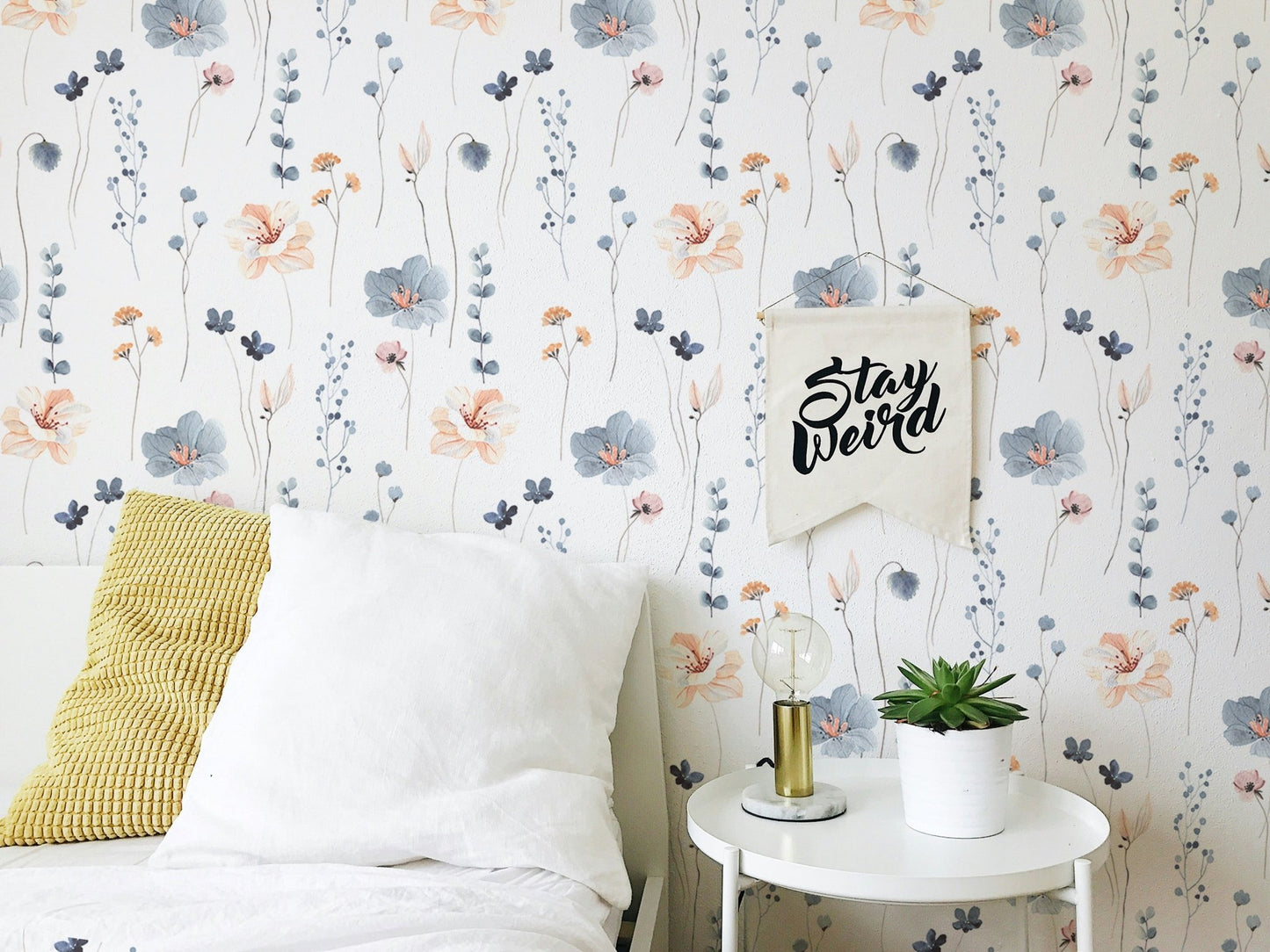 Floral leaves repeat pattern wallpaper in a bedroom with white cushions and a side table.