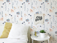 Floral leaves repeat pattern wallpaper in a bedroom with white cushions and a side table.