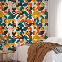 Colorful geometric wallpaper behind a bed with brown throw and white pillows.