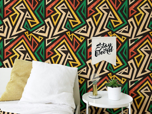 Bedside table and plant by an African geometric effect wallpaper in black and green.
