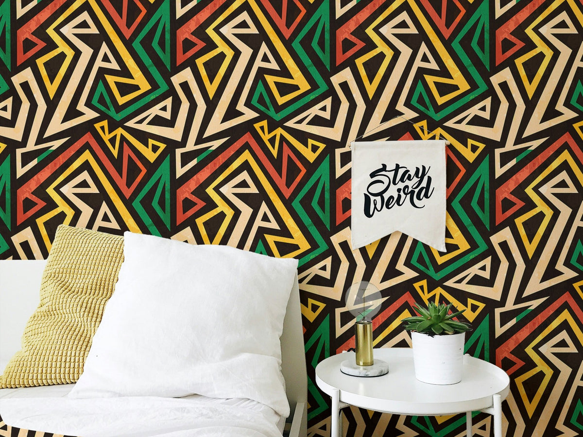 Bedside table and plant by an African geometric effect wallpaper in black and green.