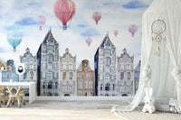 Nursery wall mural with red balloons and tall thin watercolor houses next to a white canopy.