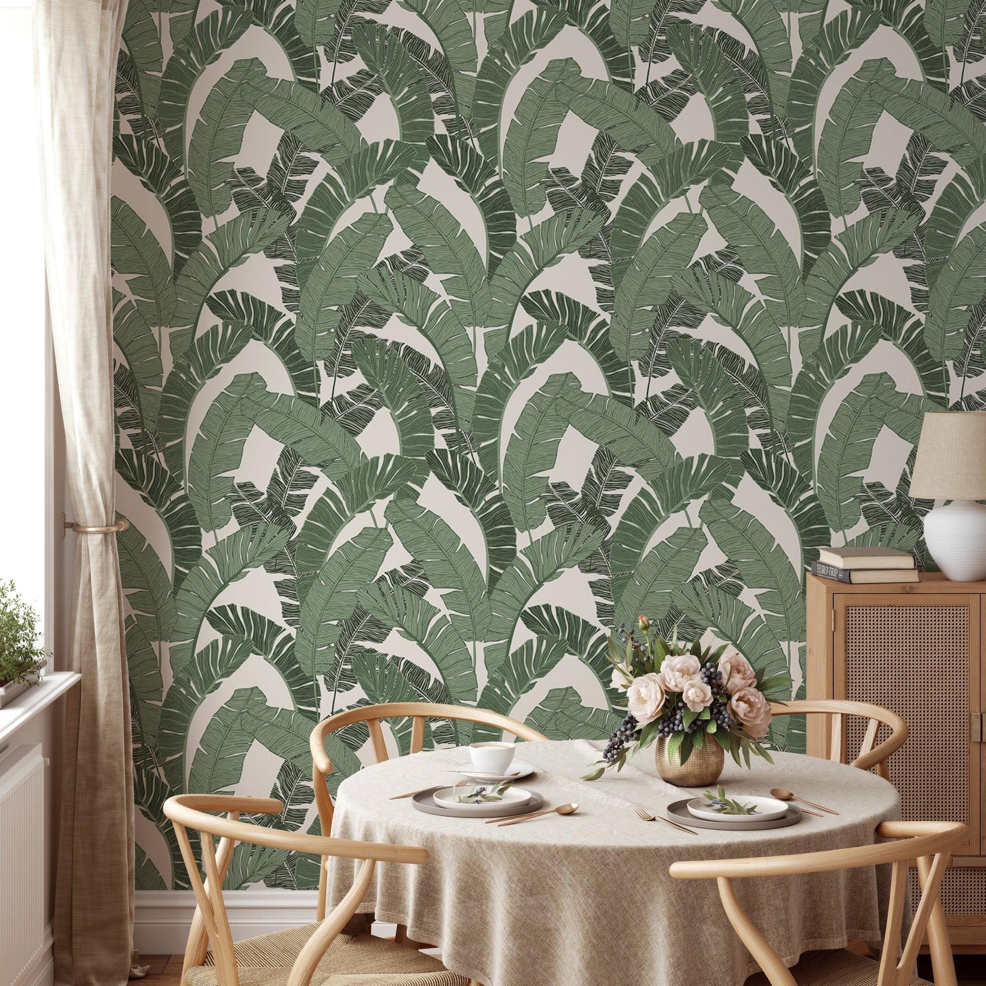 Green banana leaf wallpaper in a dining room with a round wooden table.