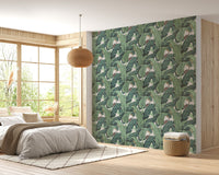 Botanical leaf print wall mural behind a bed with neutral linens and wicker lamp.