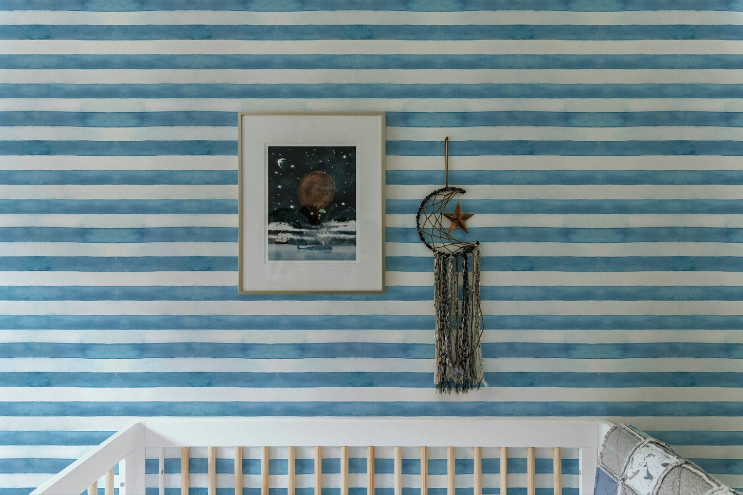 Baby crib with framed art on blue and white striped wallpaper.