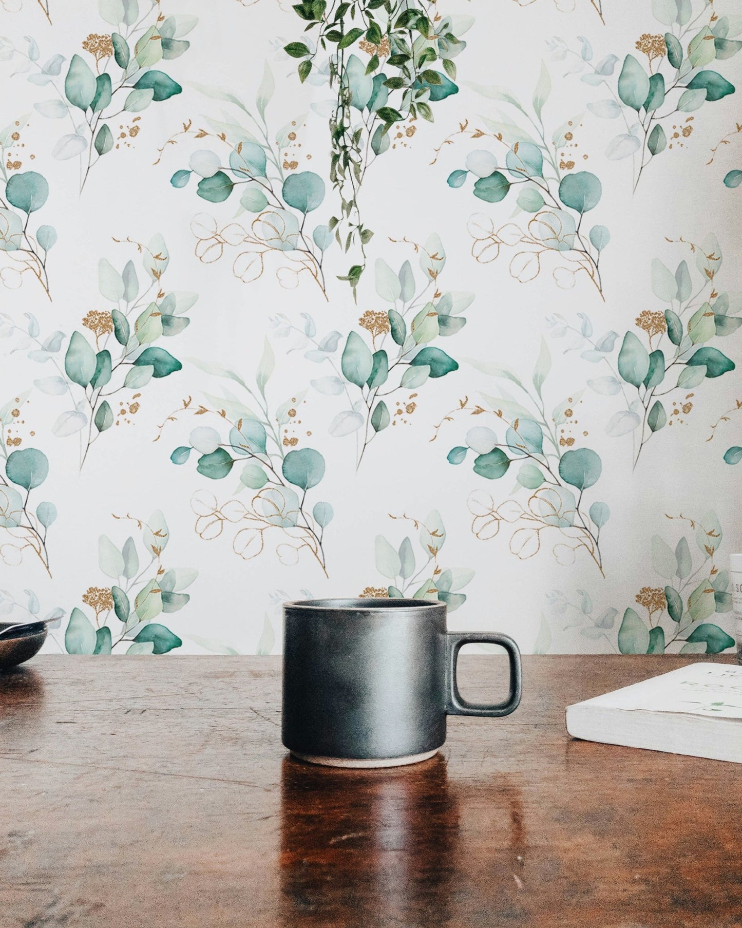 Eucalyptus leaf pattern wallpaper seen behind a wooden table with a black mug