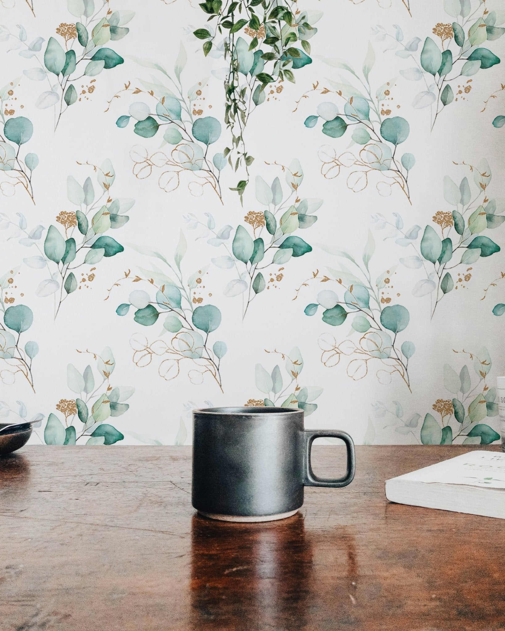 Eucalyptus leaf pattern wallpaper seen behind a wooden table with a black mug