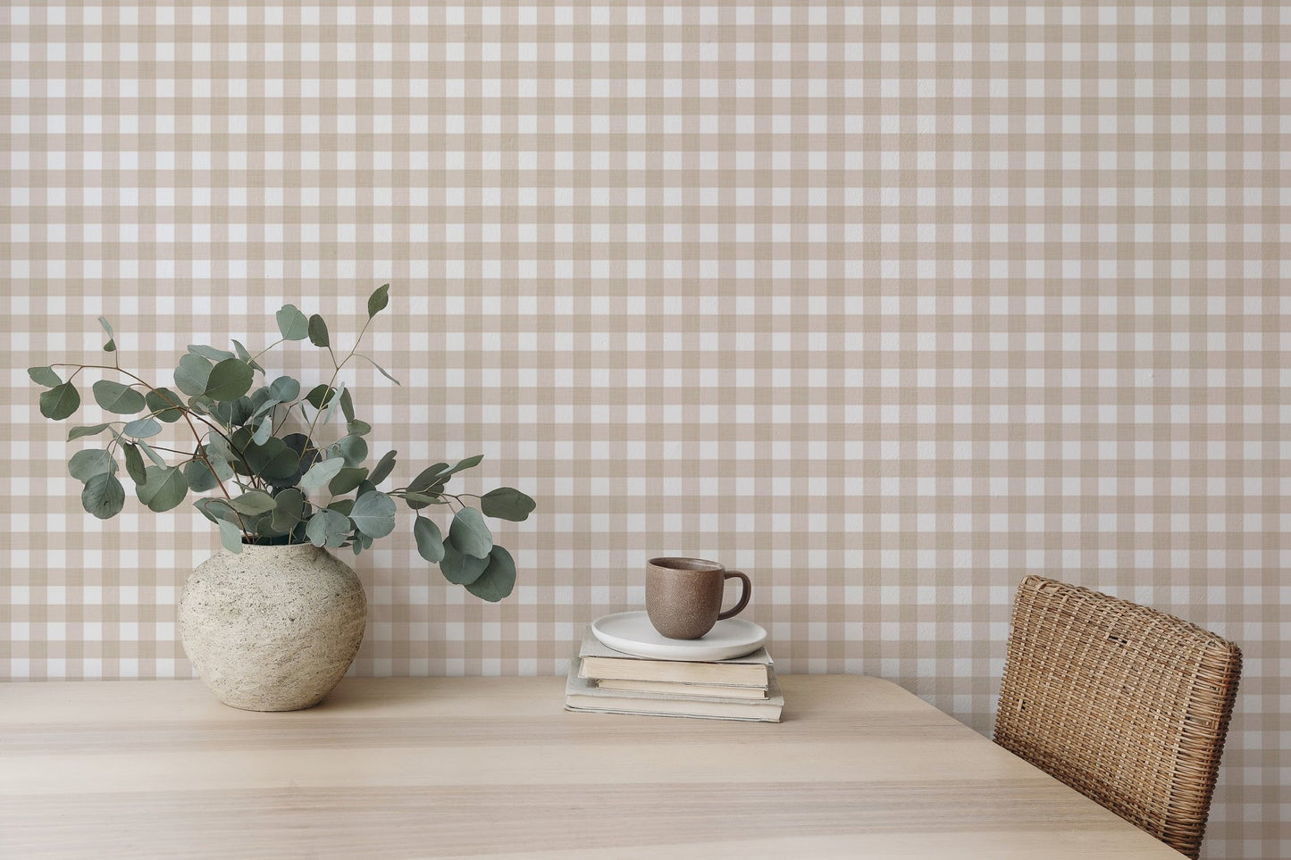 Wooden desk with a vase of leaves and beige checkered wallpaper background.