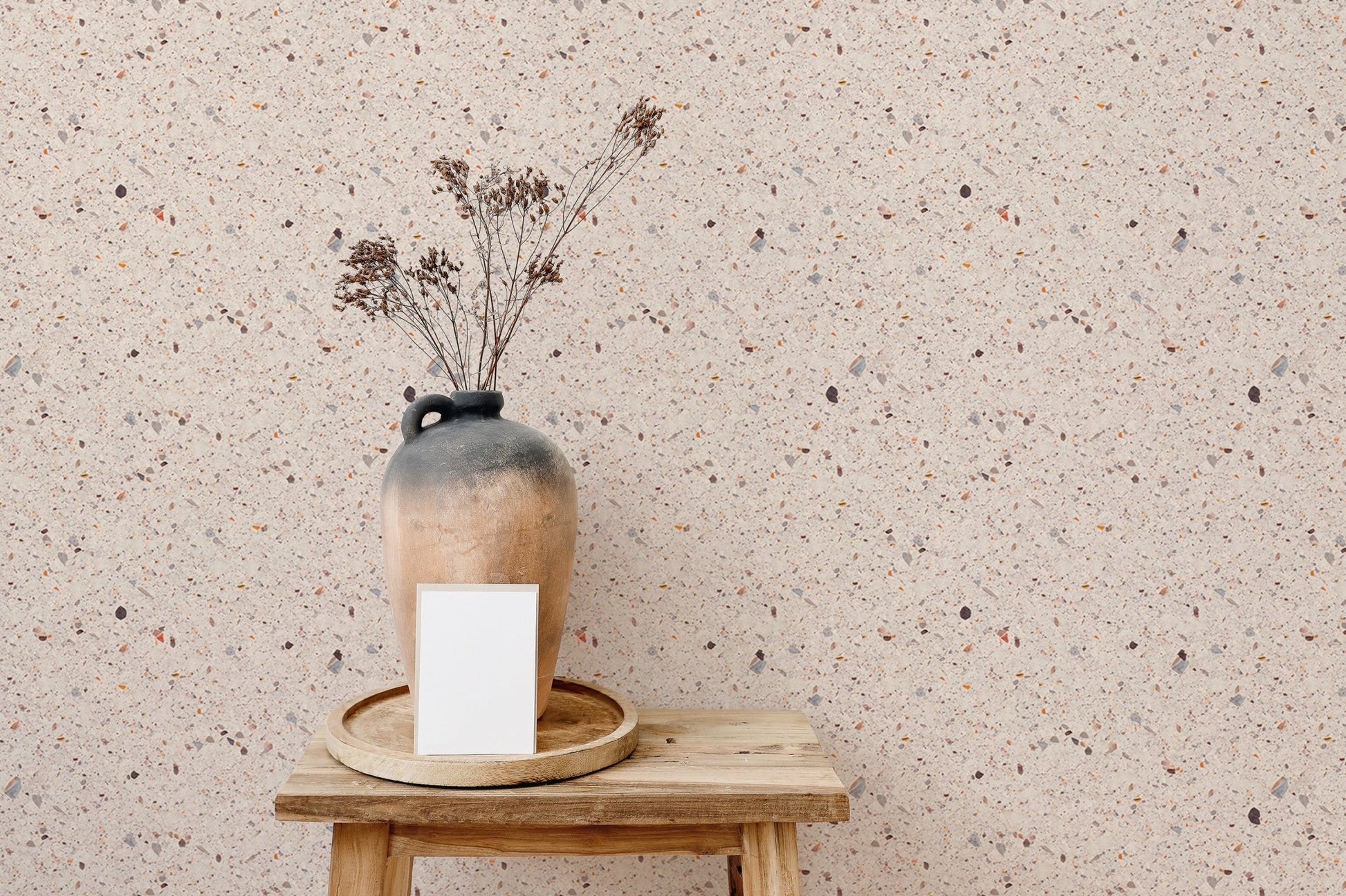Textured terrazzo wallpaper detail behind wooden stool and dry flowers.