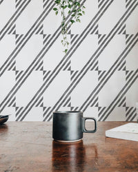 Coffee mug on a table in front of a black and white diagonal stripe wallpaper