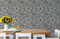 Black and white geometric wallpaper behind a wooden dining table and chairs.