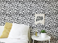 Black and white patterned wallpaper behind a bed with yellow accent pillows.