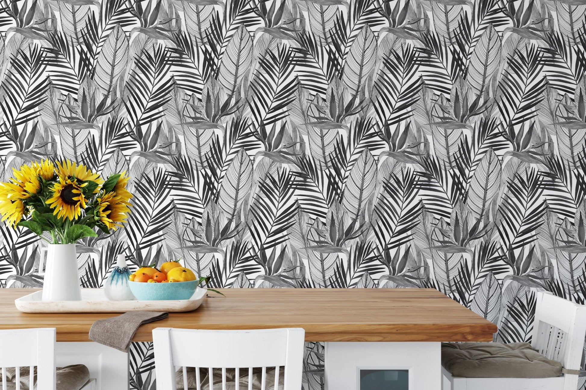 Tropical palm leaves wallpaper behind dining table with sunflowers and fruit.