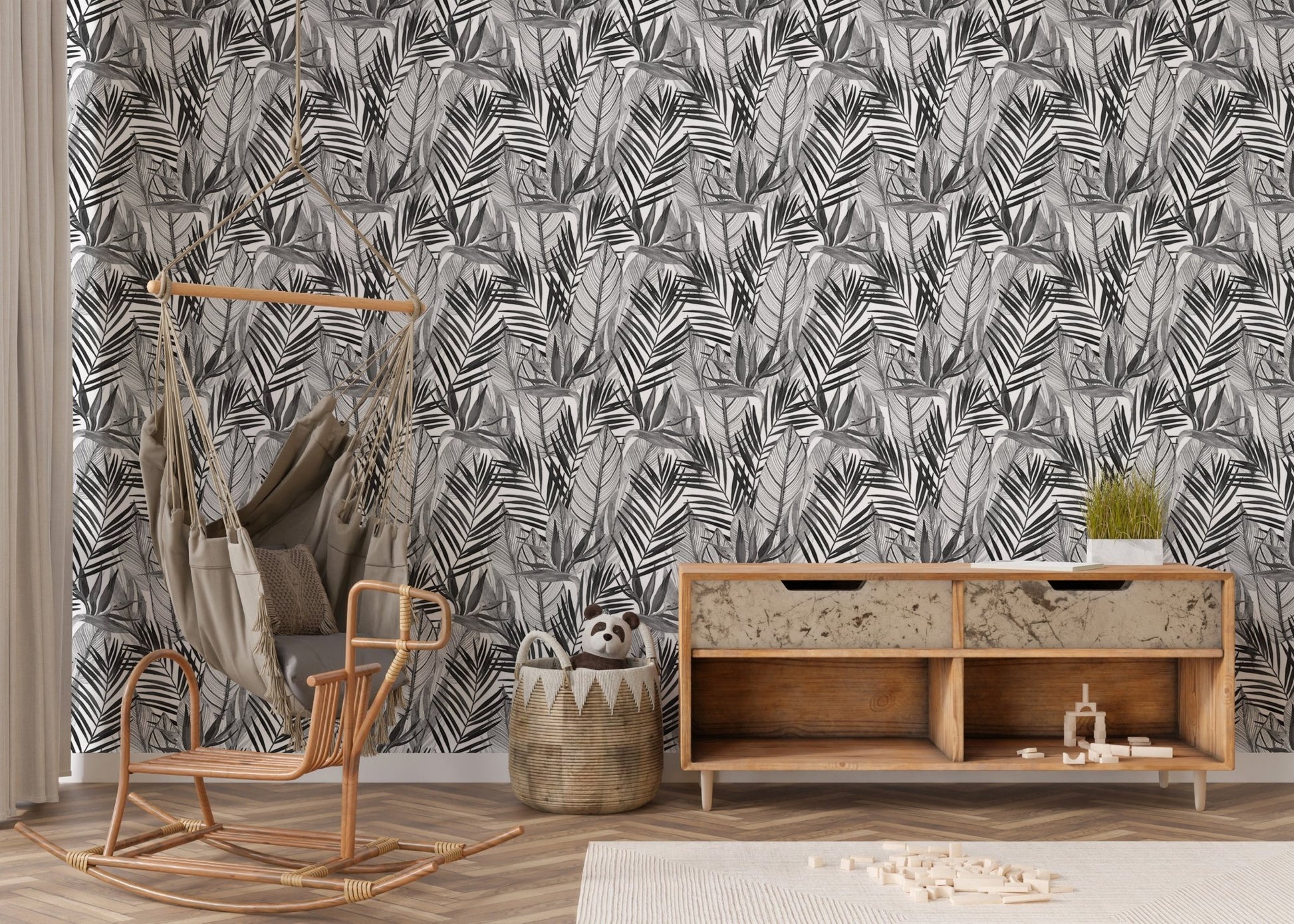 Botanical palm leaf wallpaper behind wooden sideboard and rattan chair.