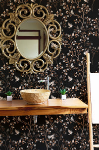 Bathroom wallpaper with black chinoiserie patterns behind a gold mirror and vanity.