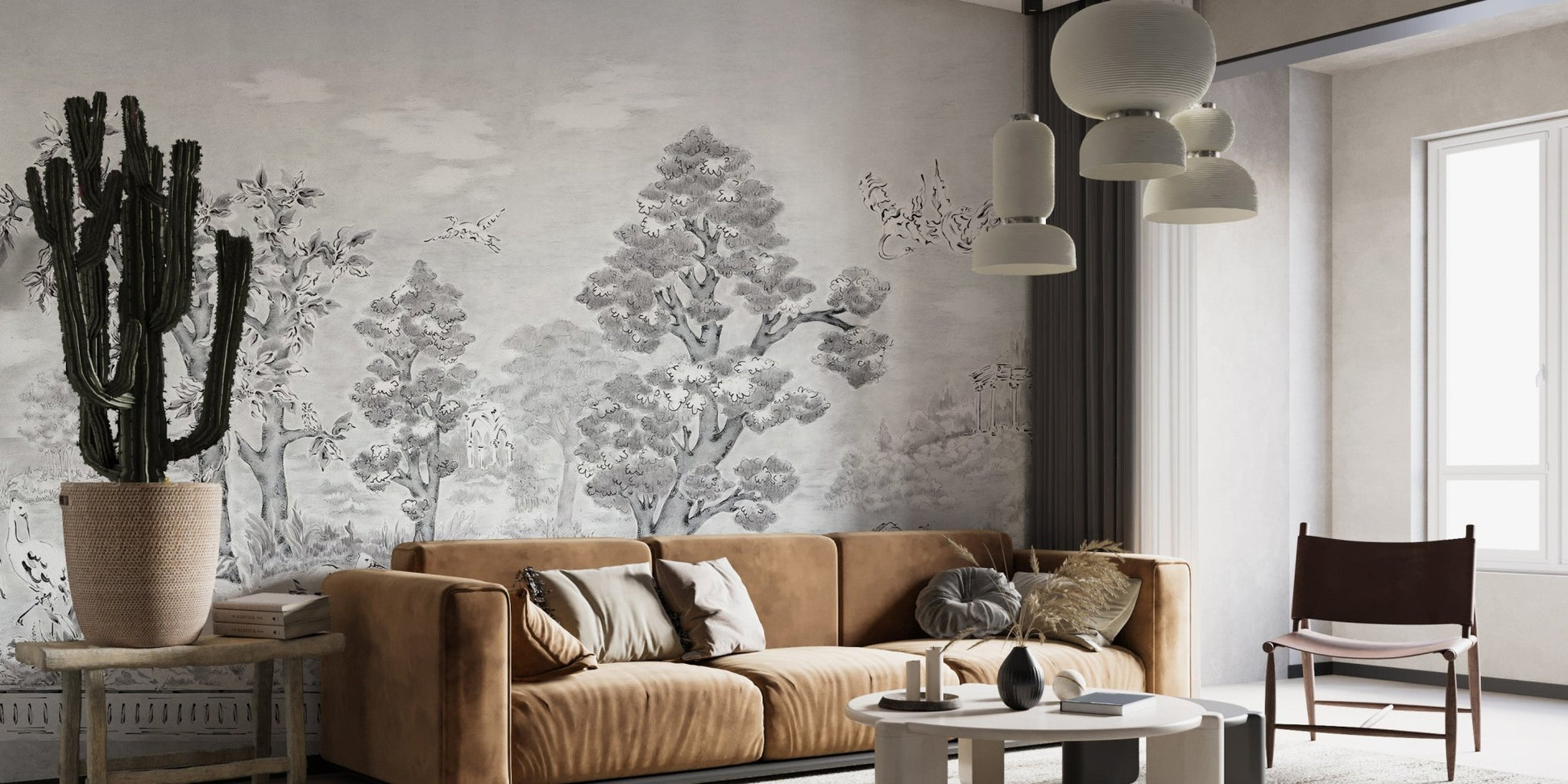 Charcoal tree sketch wall mural behind a tan leather couch and indoor plants.