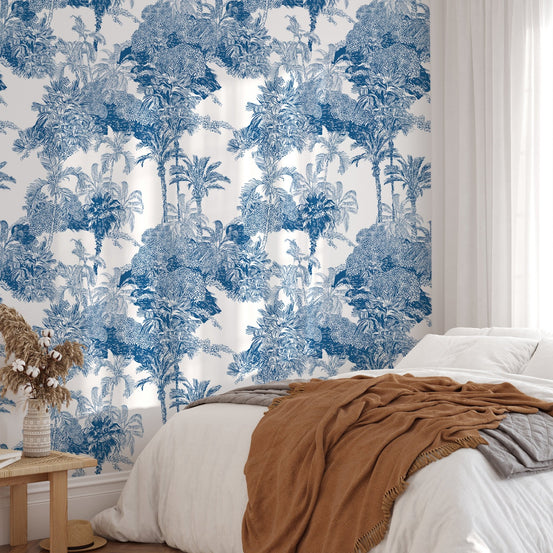 Large scale tropical wallpaper in a bedroom with brown accents and white bedding.