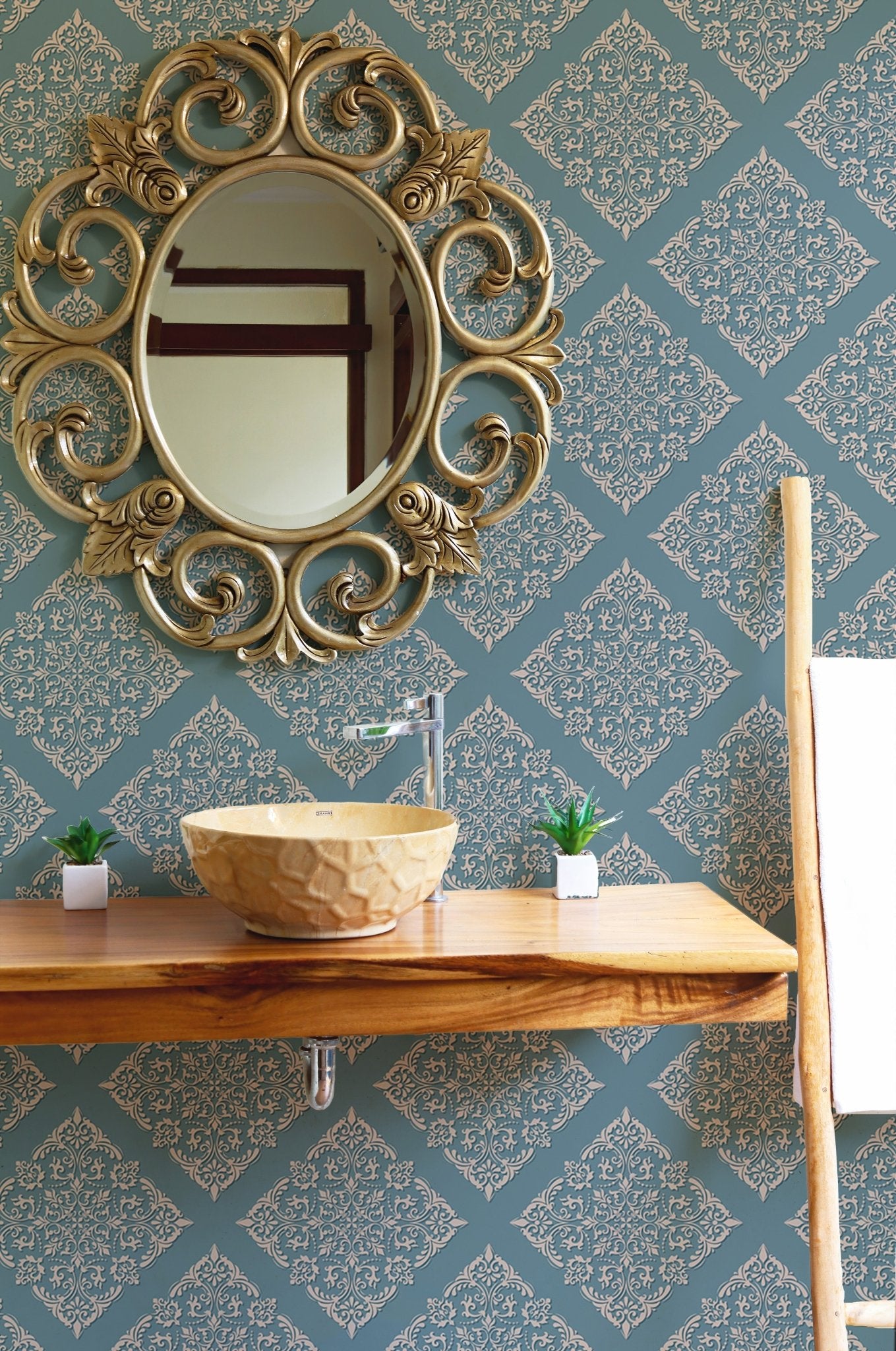 Damask wallpaper in bathroom behind wooden vanity and gold mirror.