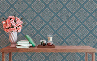 Blue patterned wallpaper in study area behind wooden table with flowers.