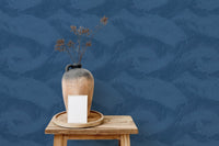 Blue tropical leaf pattern wallpaper above wooden stool with ceramic vase.