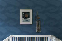 Minimalist blue palm frond wallpaper in a nursery with white crib and frame.