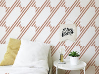 Wallpaper with brown linear patterns behind a white bed and side table.