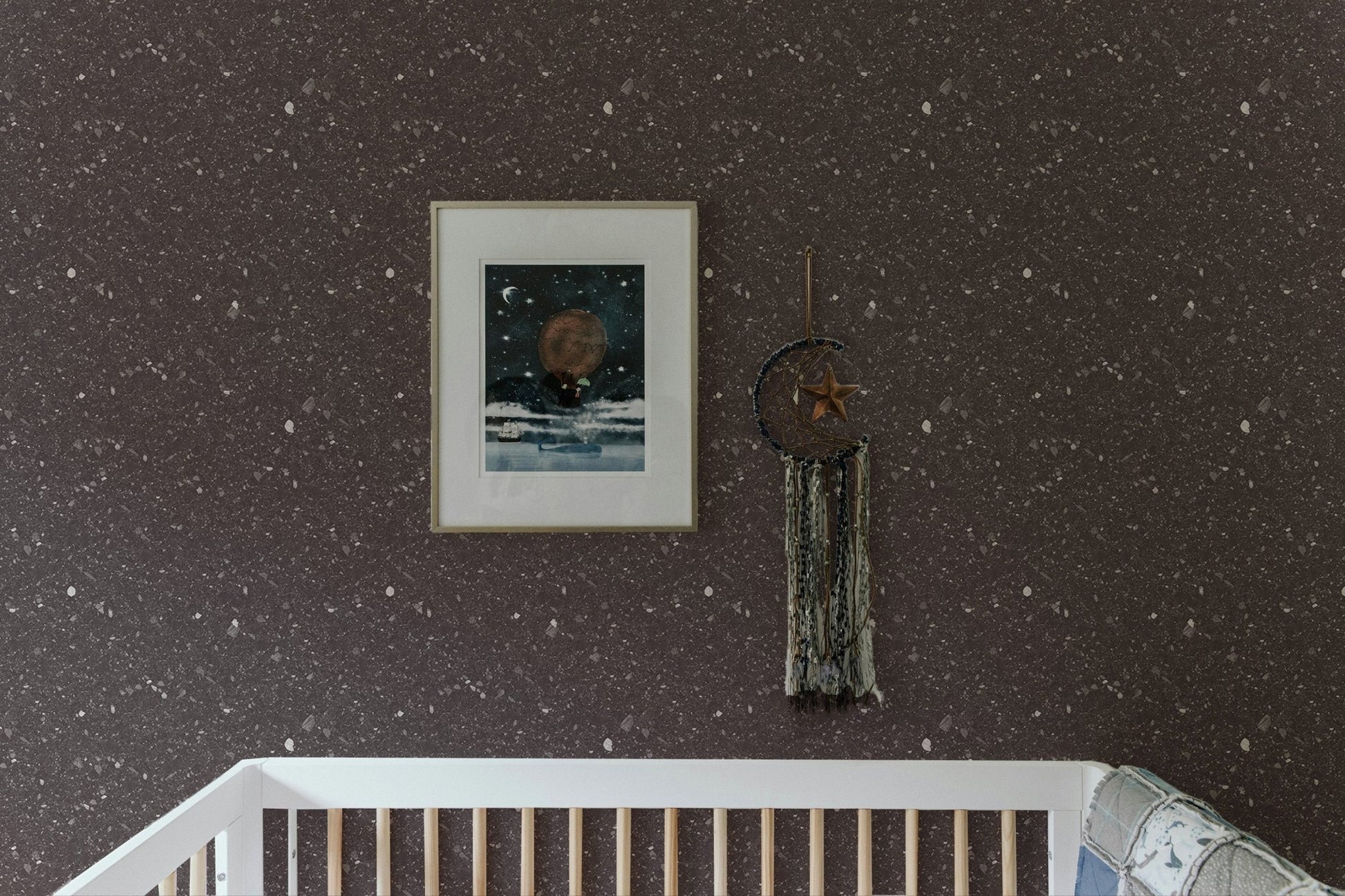 Speckled stone wallpaper in a nursery above a white wooden cot and framed art.