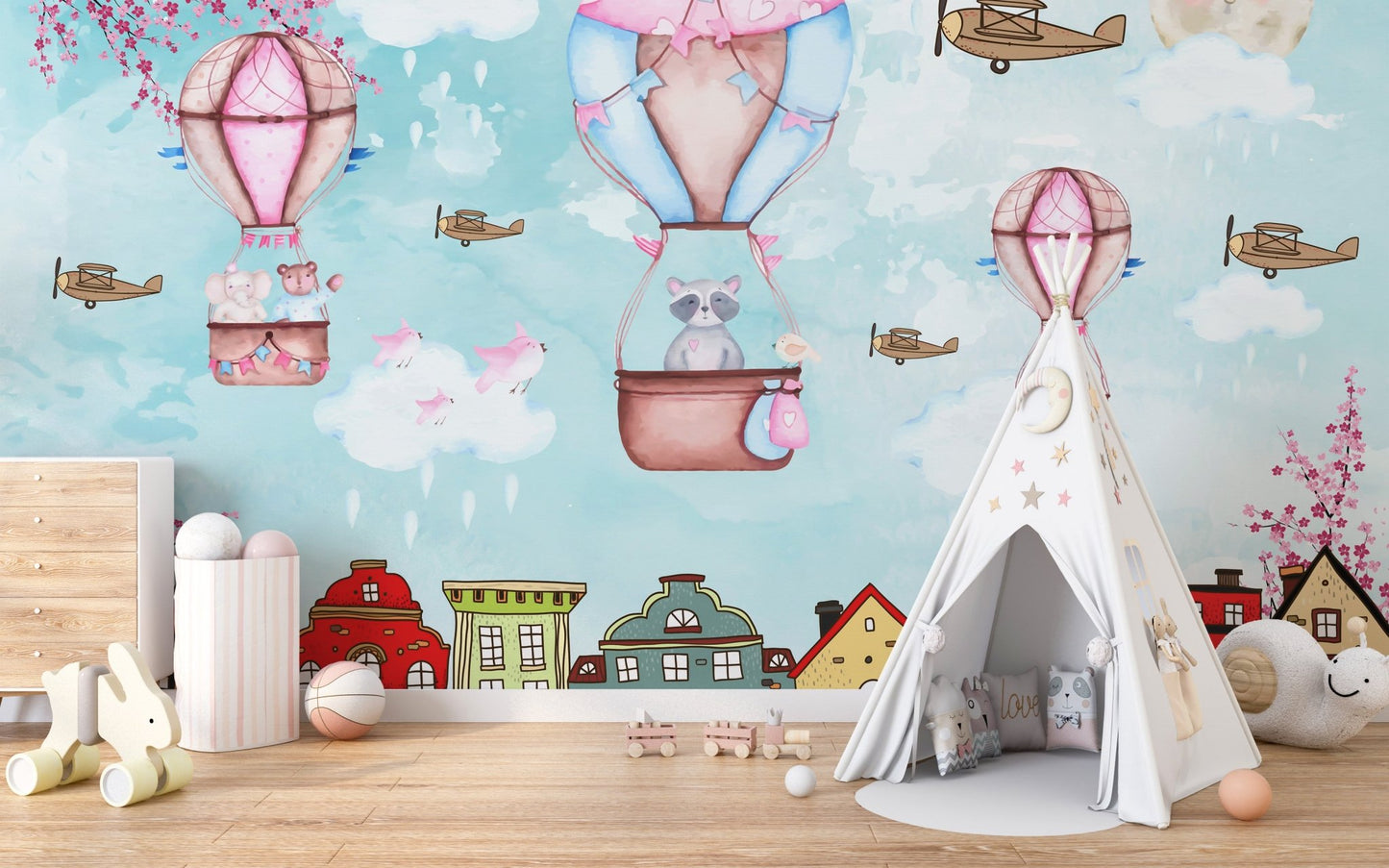 Hot air balloon aerial wall mural in a nursery with a white teepee and wooden floor.