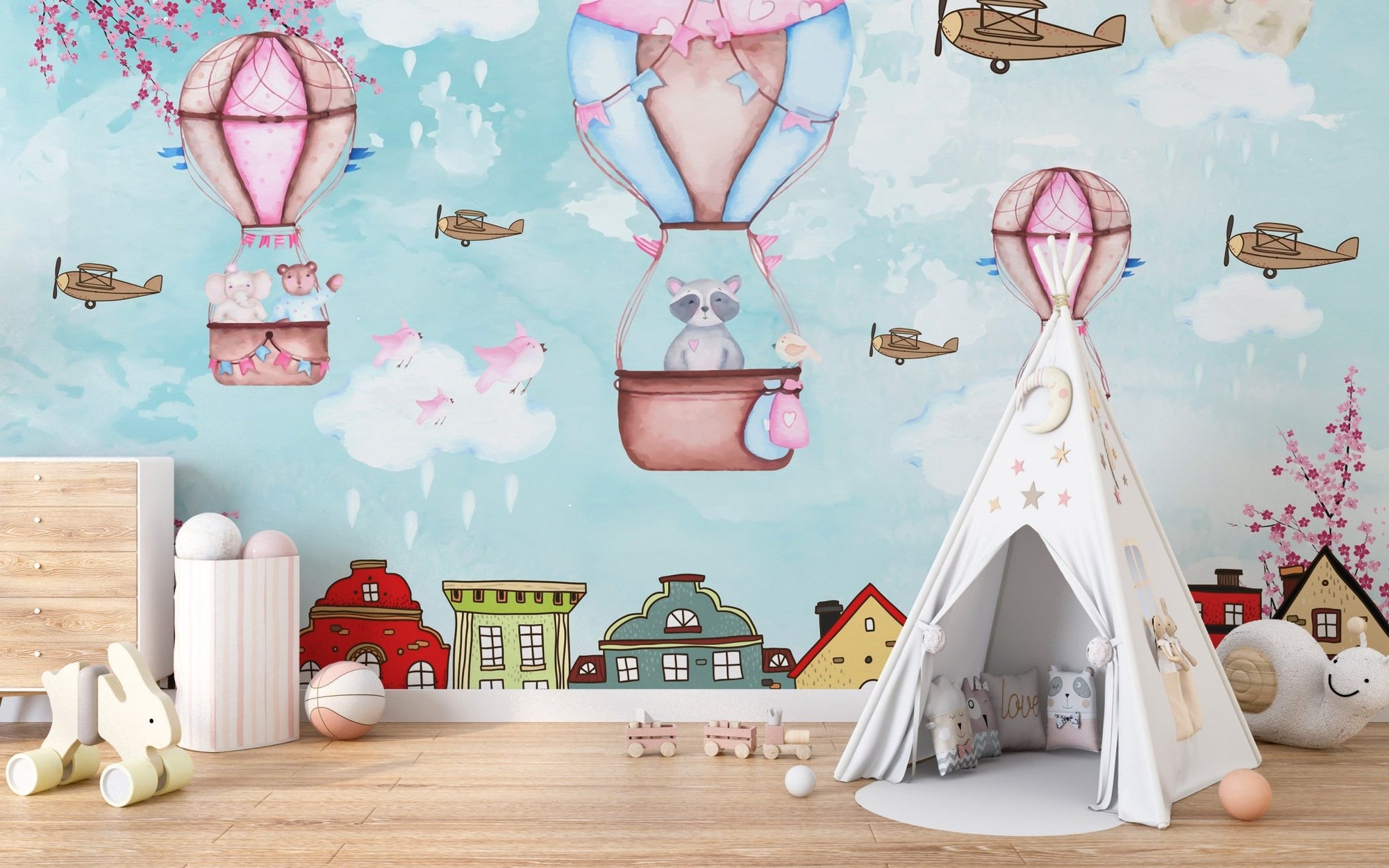 Hot air balloon aerial wall mural in a nursery with a white teepee and wooden floor.