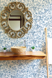 Flower wallpaper in a bathroom with a round gold mirror and wooden vanity