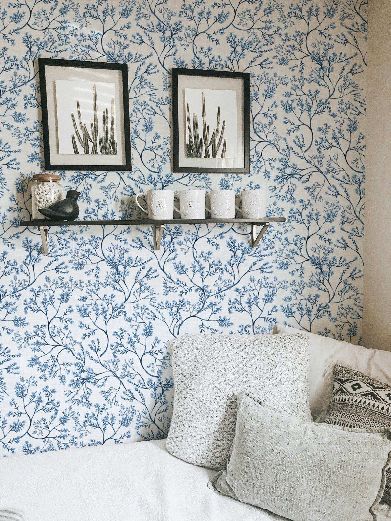 Botanical wallpaper in a small room with framed art and a white bed