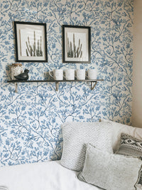 Botanical wallpaper in a small room with framed art and a white bed