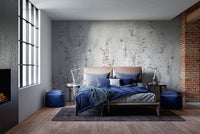 Bedroom with blue bedding and climbing floral branch wall mural on grey plaster.
