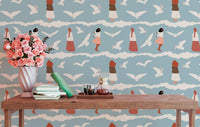 Coastal wallpaper with bird illustrations behind a wooden bench and pink flowers.