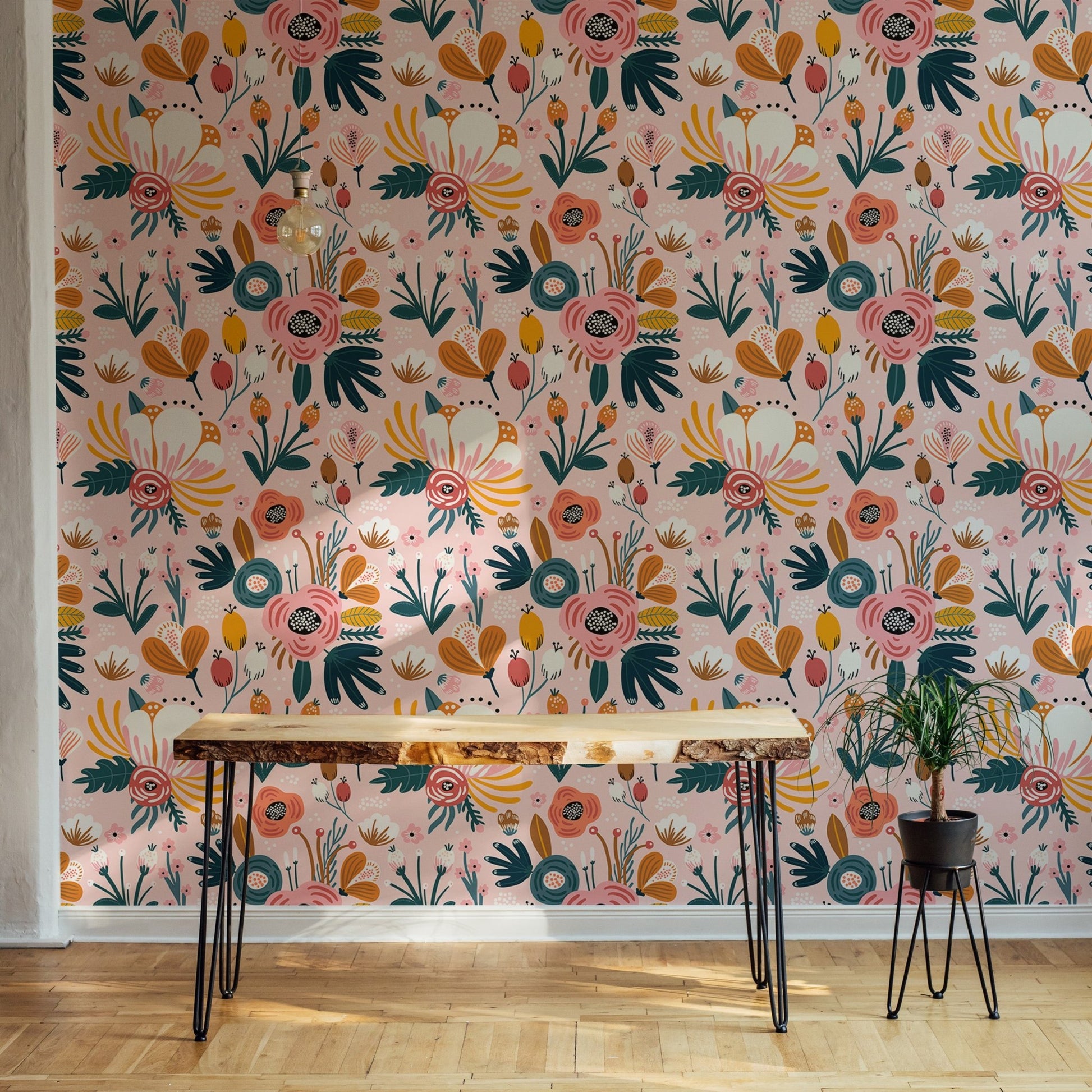 Pink floral wallpaper behind wooden desk and black metal legs in home office.