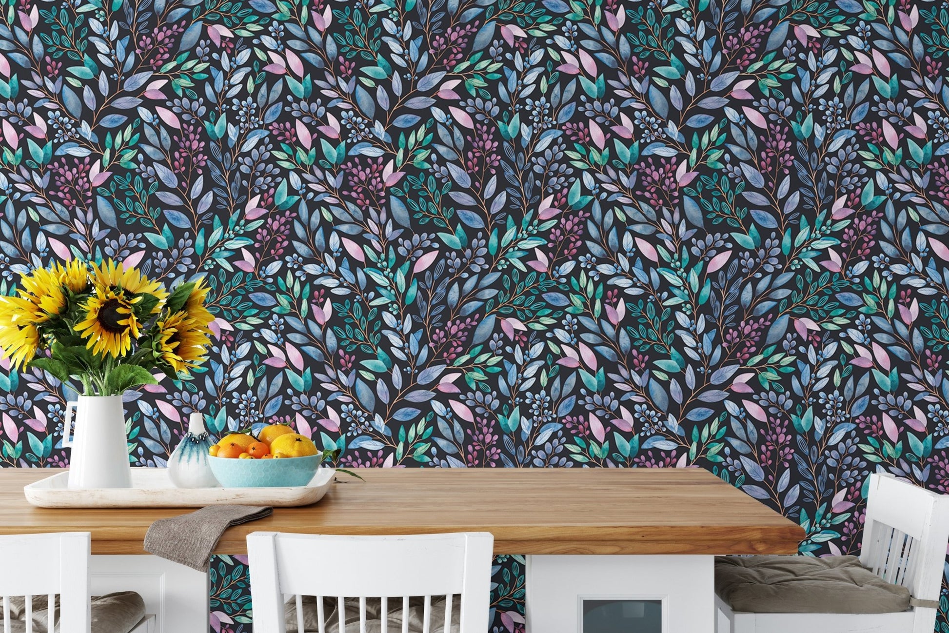 Dark floral leaves wallpaper backdrop for a wooden dining table with white chairs.