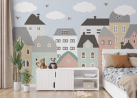 Cityscape houses wall mural behind a white unit and potted plant in a bedroom.
