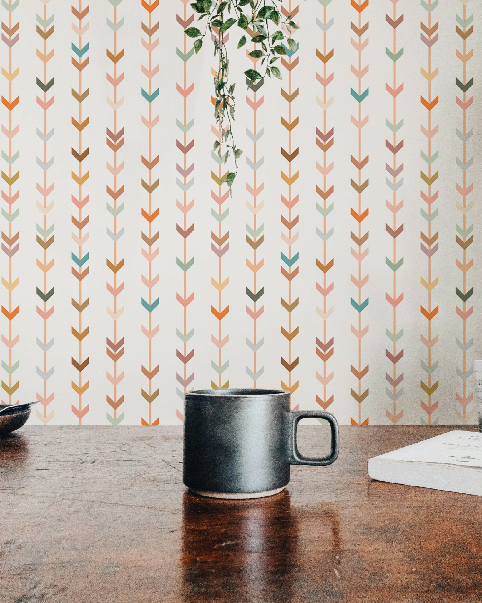 Earth tone geometric wallpaper behind a dark coffee mug on a wooden desk.