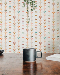 Earth tone geometric wallpaper behind a dark coffee mug on a wooden desk.