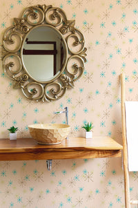 Wall mural with teal and gold flecks in a bathroom setting behind a round ornate mirror.