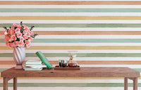 Hand-painted stripe effect wallpaper  behind a wooden bench with pink flowers in a vase.