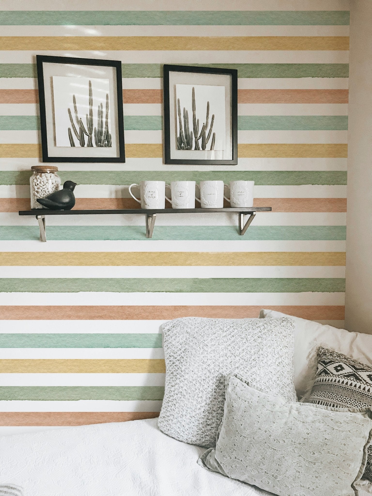 Horizontal pastel stripes wallpaper behind a white bed with black framed art