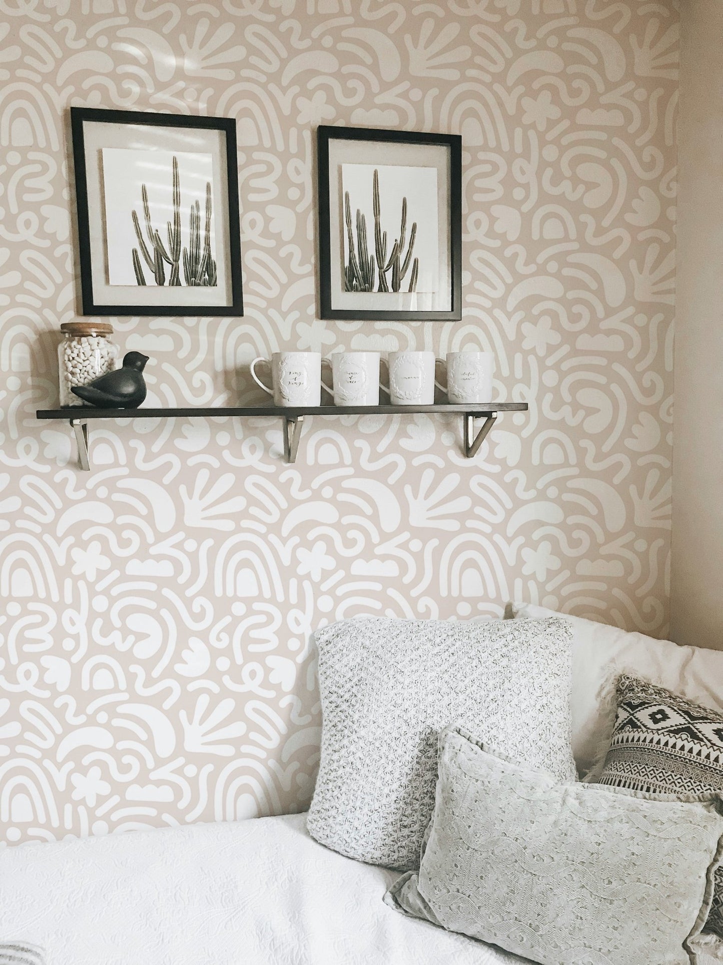 Scandinavian wallpaper pattern in a bedroom with grey pillows and black frames.