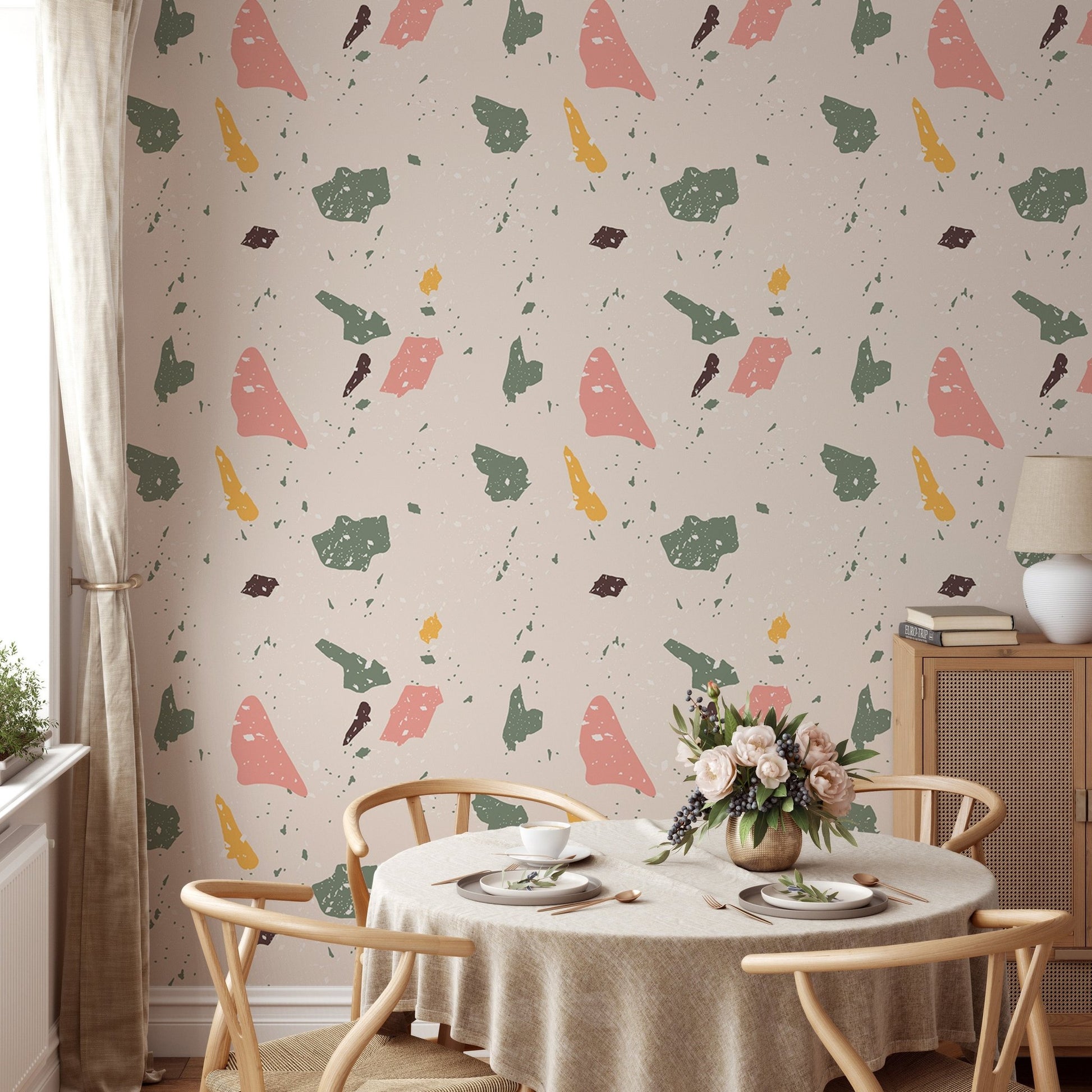 Terrazzo wallpaper with pink and green shapes behind a round dining table and chairs.
